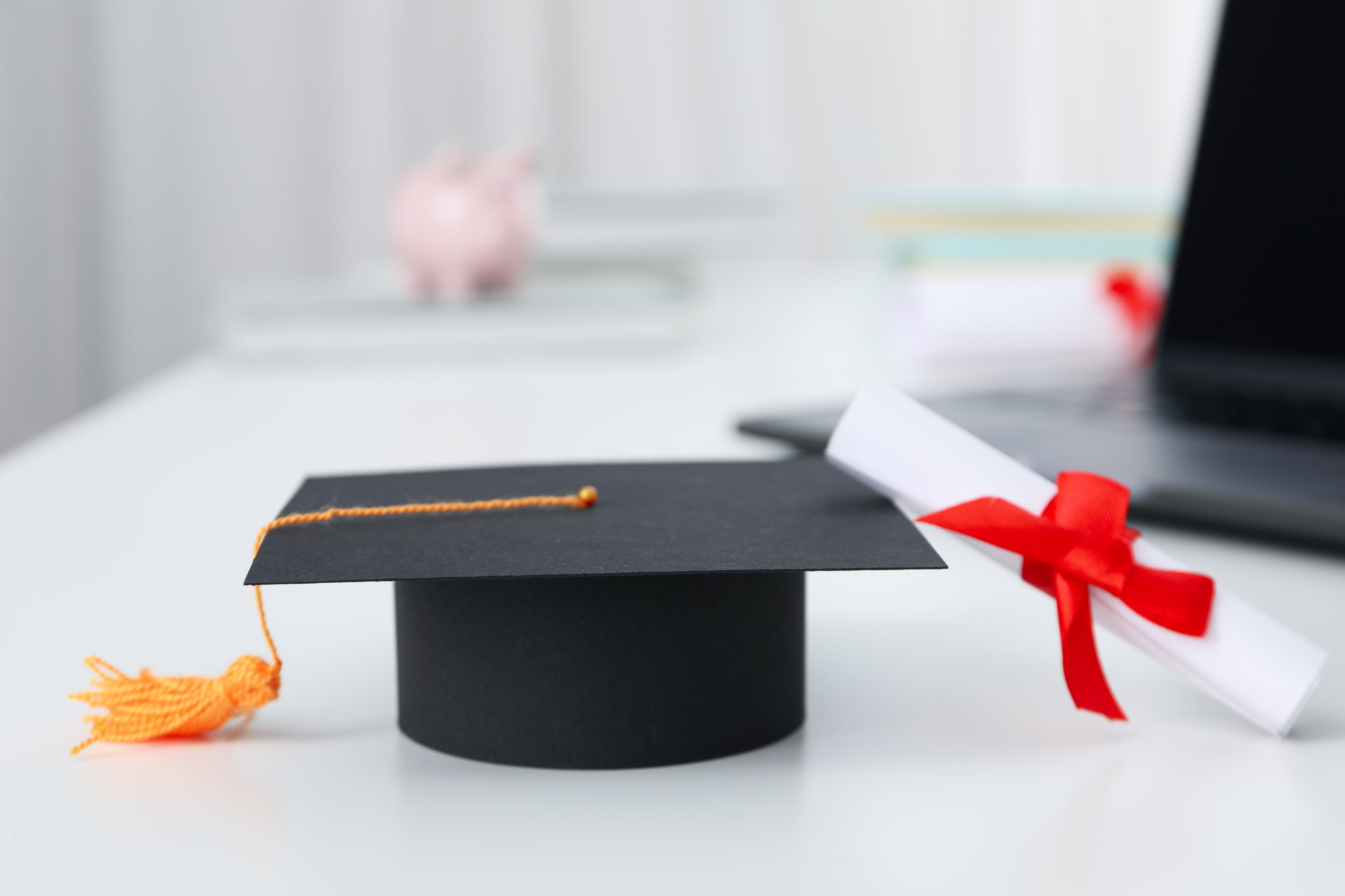 A graduation cap, diploma and laptop on a desk